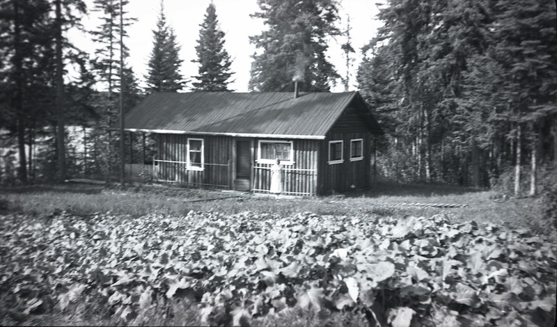 The caretaker’s wife stands in front of Robert Fitzsimmons’s house at Bitumount, ca. 1930s, where she can see the extensive vegetable garden in the foreground.
