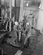 These men are soaked in mud, or drilling fluid, which is essential to the fluid circulation system and serves the functions of cooling and lubricating the drill bit, flushing out cuttings, controlling well pressure and sealing the well walls.  The earliest drilling fluid was simply water, but in the 1920s, technical investigations of drilling mud began in order to determine what kind of fluid is most effective under particular conditions. Drilling muds now might be water-, oil- or synthetic-based and can provide different solutions within a well. Source: Provincial Archives of Alberta, PA 412/7