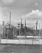 Liquid sulfur flows into a holding area to cool and solidify below the sulfur plant seen in the background, 1952; the venting of poisonous hydrogen sulfide gas into the atmosphere was banned in 1952, rendering obsolete the tall silver stacks of the scrubbing plant at left. <br />Source: Provincial Archives of Alberta, P2987