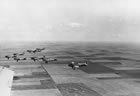 Eight training aircraft, likely Fairchild Cornells, based out of No. 5 Elementary Flying Training School in High River, Alberta, flying in formation, ca. 1941-1945. The British Commonwealth Air Training Plan saw the construction of dozens of airfields for the training of Allied pilots during the Second World War. The training plan was one of Canada’s major contributions to the war effort. The hundreds of aircraft and daily training flights required vast quantities of aviation fuel, which Turner Valley helped to provide. <br />Source: Glenbow Archives, NA-4943-3