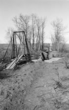 Most of Turner Valley’s pipelines are buried, but some landforms required other solutions, as here, where a suspension bridge was constructed to carry a 15cm (6 in.) pipeline over water, May 1938. <br />Source: Glenbow Archives, IP-6e-1-57