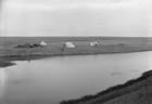 Surveyors’ tents are erected alongside a river on a treeless plain with horse feed stacked to the left, ca. 1890s. Camps such as this were typical of both the Boundaries Commission and the Geological Survey of Canada. <br />Source: Glenbow Archives, NC-22-19