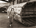 A female bucketwheel operator poses for a photograph in front of her massive machine at Syncrude oil sands mine, Fort McMurray, 1992. Once largely a male-dominated preserve, opportunities for women in all aspects of the petroleum sector are increasing. <br/>Source: Lawrence Chrismas, <em>Delores MacLean, Bucketwheel Operator, Syncrude Oilsands Mine, Fort McMurray,</em> black and white contact print <br/>Collection of the Alberta Foundation for the Arts