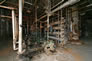 Interior of gasoline plant, showing pumps at left, distillation unit (large horizontal pipes) at centre, and refractionation tower in the background at right, ca. 2010; this equipment was used to separate ethane and propane from the rich oil produced by the absorption plant. Once these were stripped, the resulting lean oil was pumped back to the absorption plant by pumps in the lean oil pump house. <br/>Source: Alberta Culture and Tourism