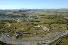 In this aerial view of the Turner Valley Gas Plant Historic Site, 2007, the community of Turner Valley can be seen in the distance. A berm, completed in 2007, protects the site from flooding by the Sheep River. A gas seep, visible as an orange flame near the far left end of the berm, burns constantly. A water treatment facility, at the far right end of the berm, collects groundwater and run-off from the site and treats it before releasing it into the river. <br />Source: Alberta Culture and Tourism, AB070914316