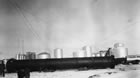 Oil and gasoline storage tanks at the Royalite’s Turner Valley gas plant, 1932; expanded capacity at the plant created a need for more storage. The long black pipe in the foreground is one of the plant’s absorption towers prior to being raised to its vertical position. <br />Source: Glenbow Archives, NA-5290-14