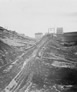 Dragline cables for pulling the bucket up the hill were attached to the metal structure silhouetted against the sky (centre), International Bitumen Company, after 1937.<br/>Source: University of Alberta Archives, 83-160-0